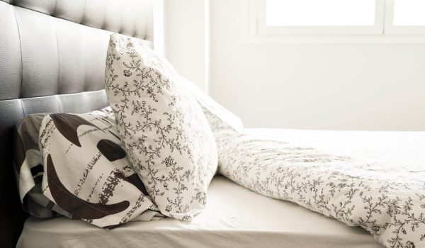 A bed with a patterned comforter with two pillows and a black backrest in a white room.